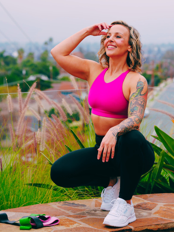 A woman in pink shirt and black pants squatting on ground.